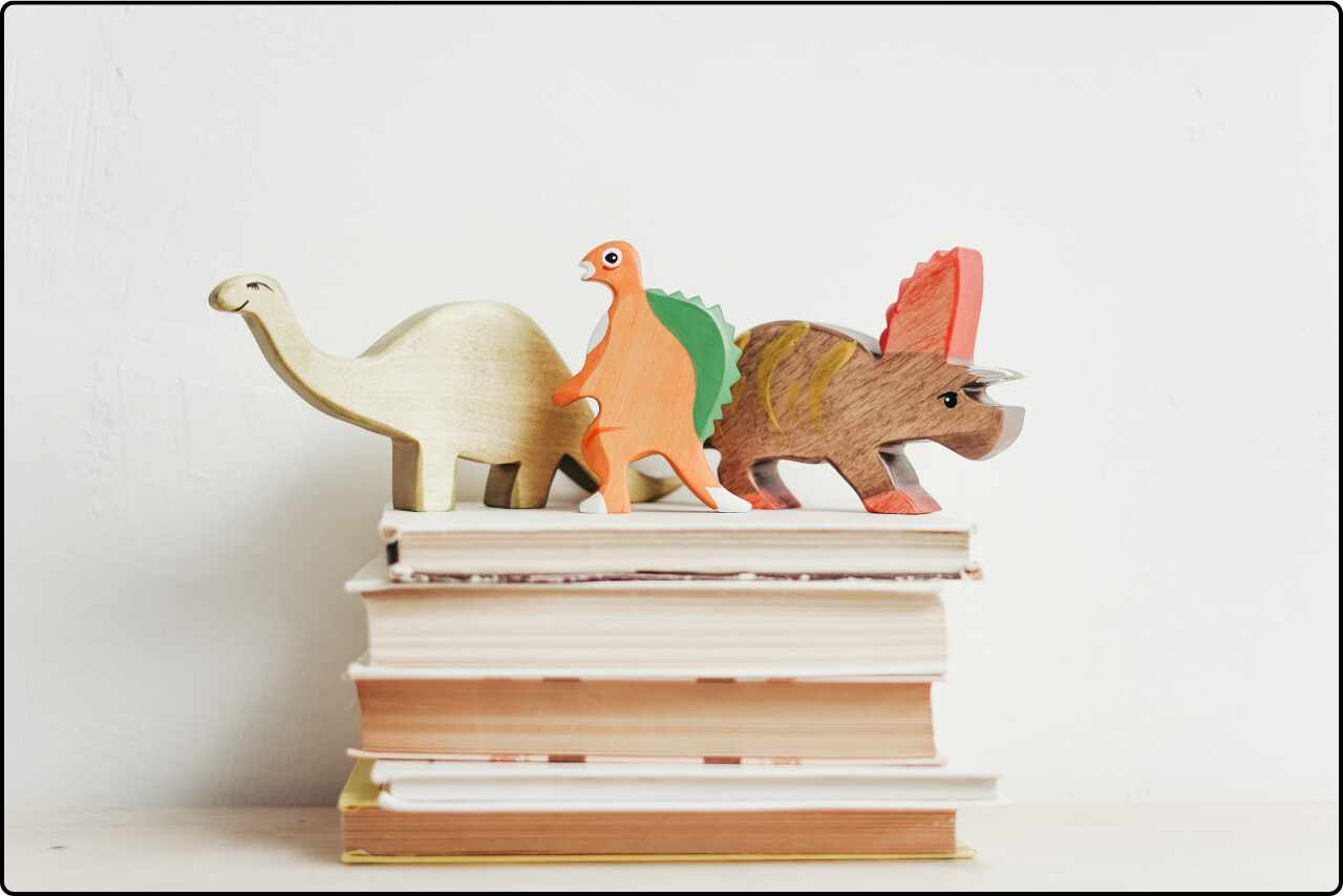 Three wooden dinosaurs placed on top of a book.